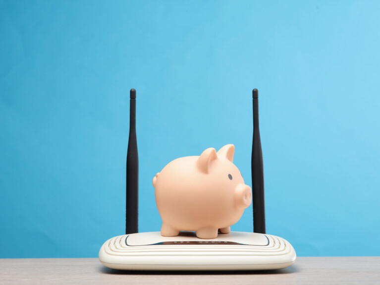 Dual antenna wi-fi router with piggy bank on the table, blue background